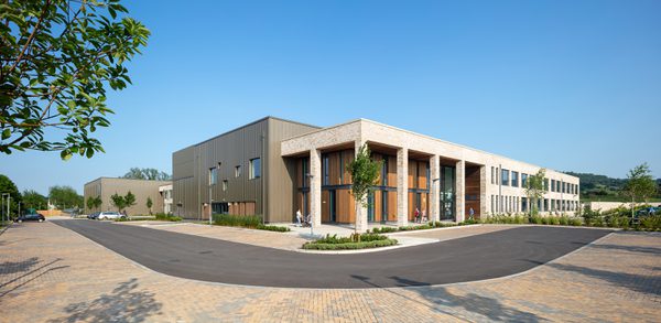 An exterior view of the High School Leckhampton, showing the scale of the school in its entirety, with hard landscaped area and planting surrounding.