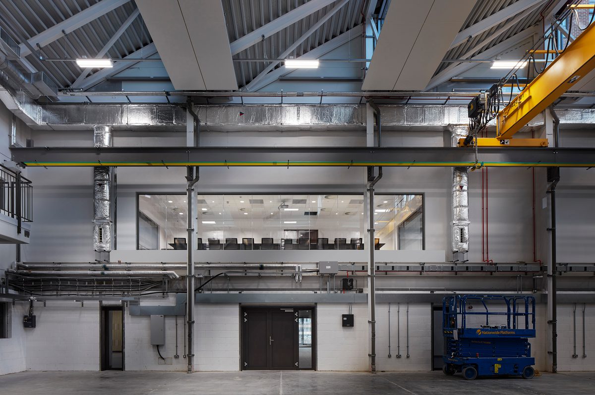 Industrial interior within the IMPACT building, with exposed beams, overhead crane, and a mezzanine level overlooking equipment.