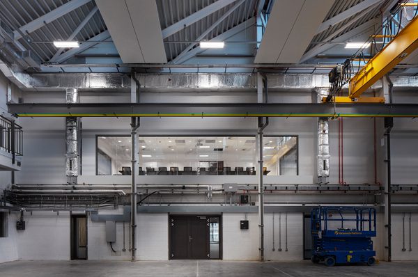Industrial interior within the IMPACT building, with exposed beams, overhead crane, and a mezzanine level overlooking equipment.