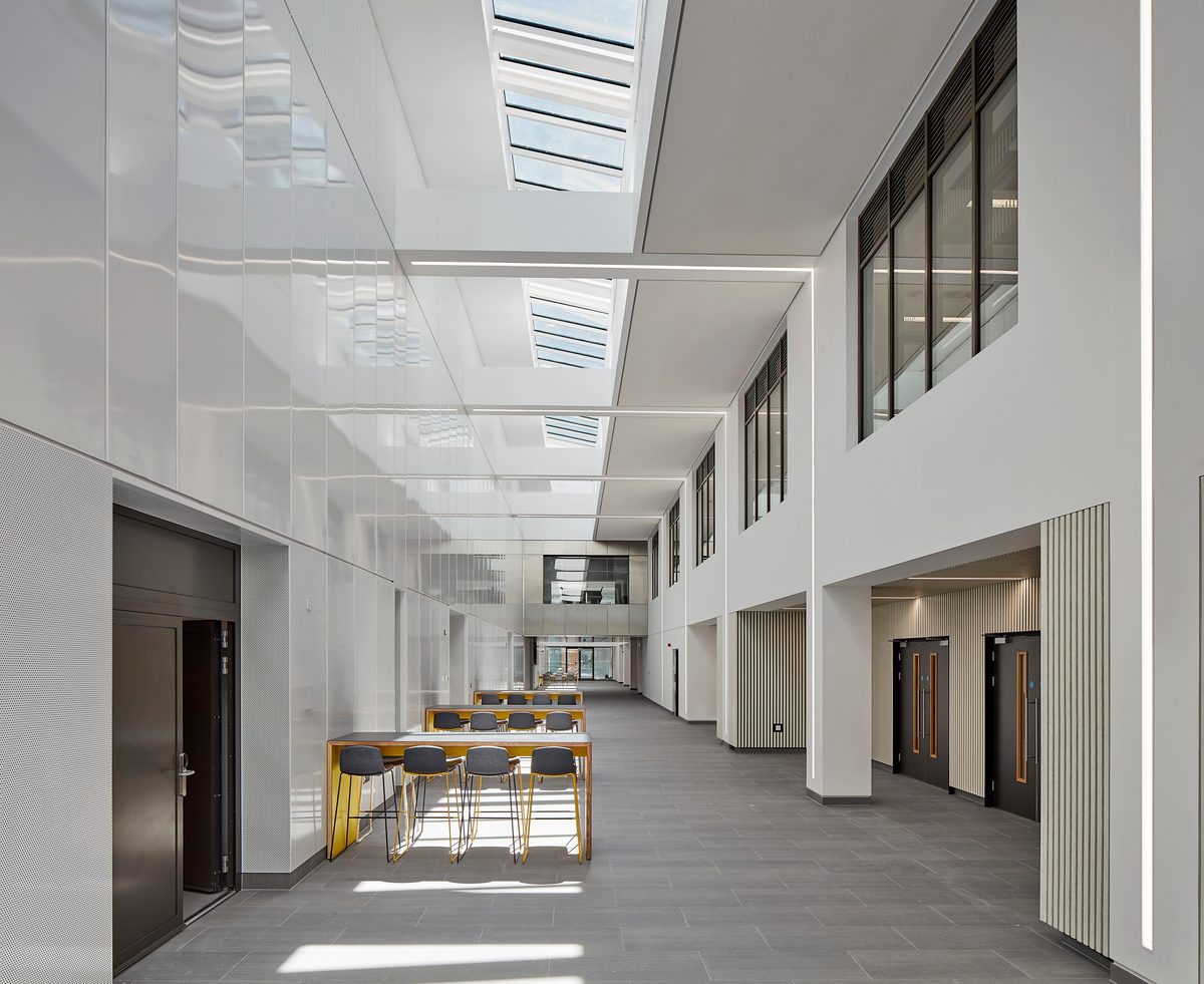 Bright, modern atrium within the IMPACT building, with white walls, skylights overhead, and a central seating area with yellow chairs
