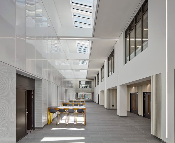 Bright, modern atrium within the IMPACT building, with white walls, skylights overhead, and a central seating area with yellow chairs
