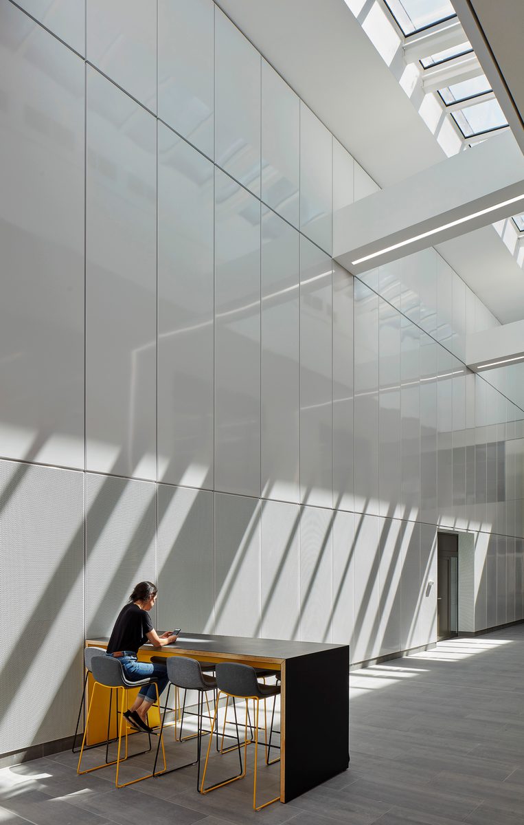 A person sitting at a high table in the bright, modern IMPACT building with tall white panelled walls and skylights welcoming in an abundance of natural light.