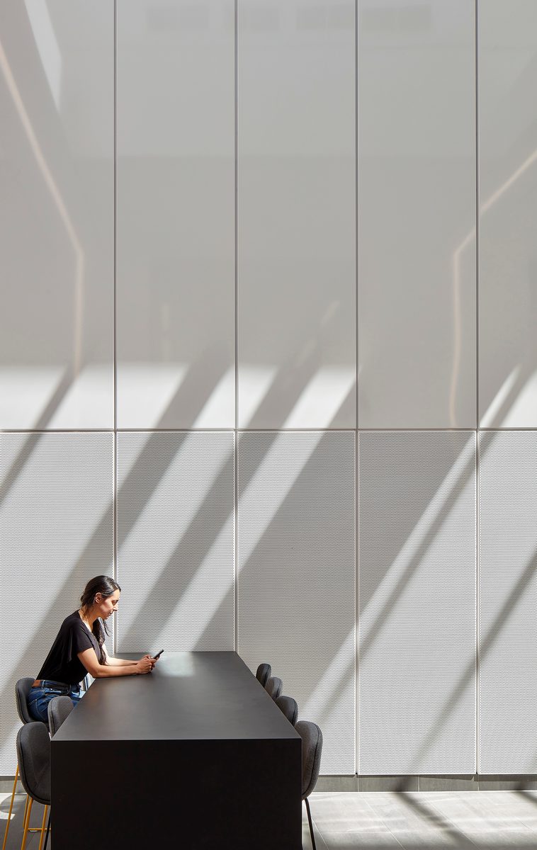 A person sitting alone on a communal table in a bright atrium space, within the IMPACT building.