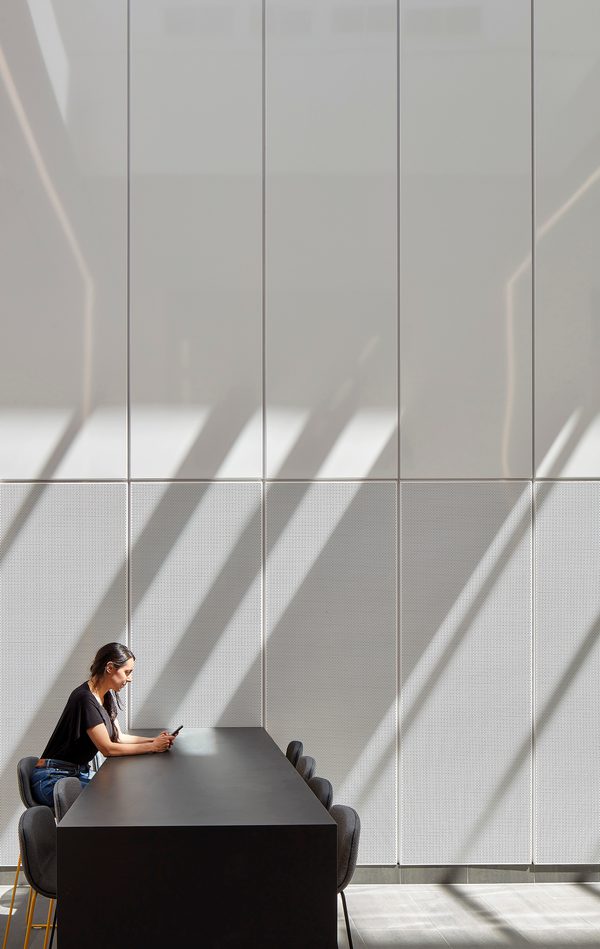 A person sitting alone on a communal table in a bright atrium space, within the IMPACT building.