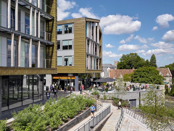 An exterior side veiw of Keynsham Civic Centre and One-Stop-Shop with people using the green spaces and surrounding public realm.