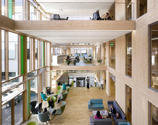 Bright multi level atrium of the Keynsham Civc Centre, with one glazed wall, wooden cladding and people working in a variety of different workspaces.