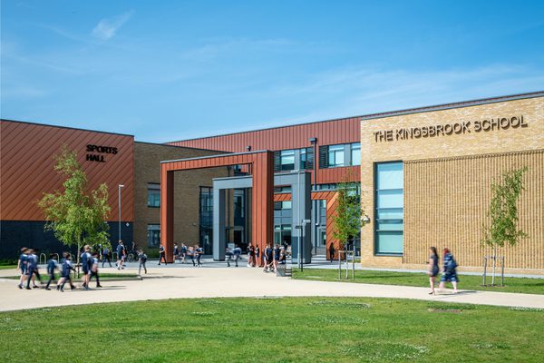 The front entrance to Kingsbrook Secondary School with students walking around and planting.