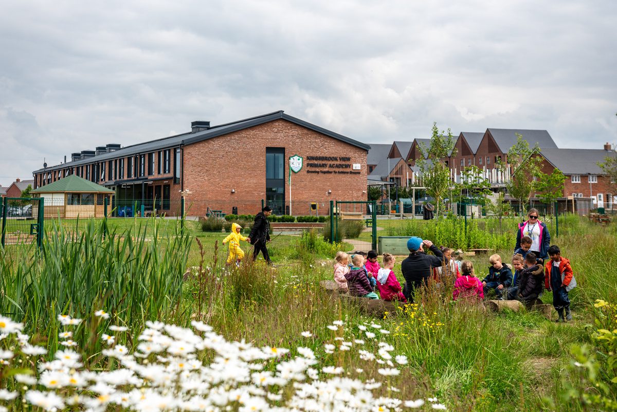 Children enjoying an outdoor lesson in a highly landscaped green space at Kingsbrook View Primary Academy, surrounded by flowers and planting.