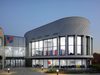 The exterior entrance at dusk of Landau Forte Academy, with double height glazing, grey cladding and academy name and logo sign on the wall.