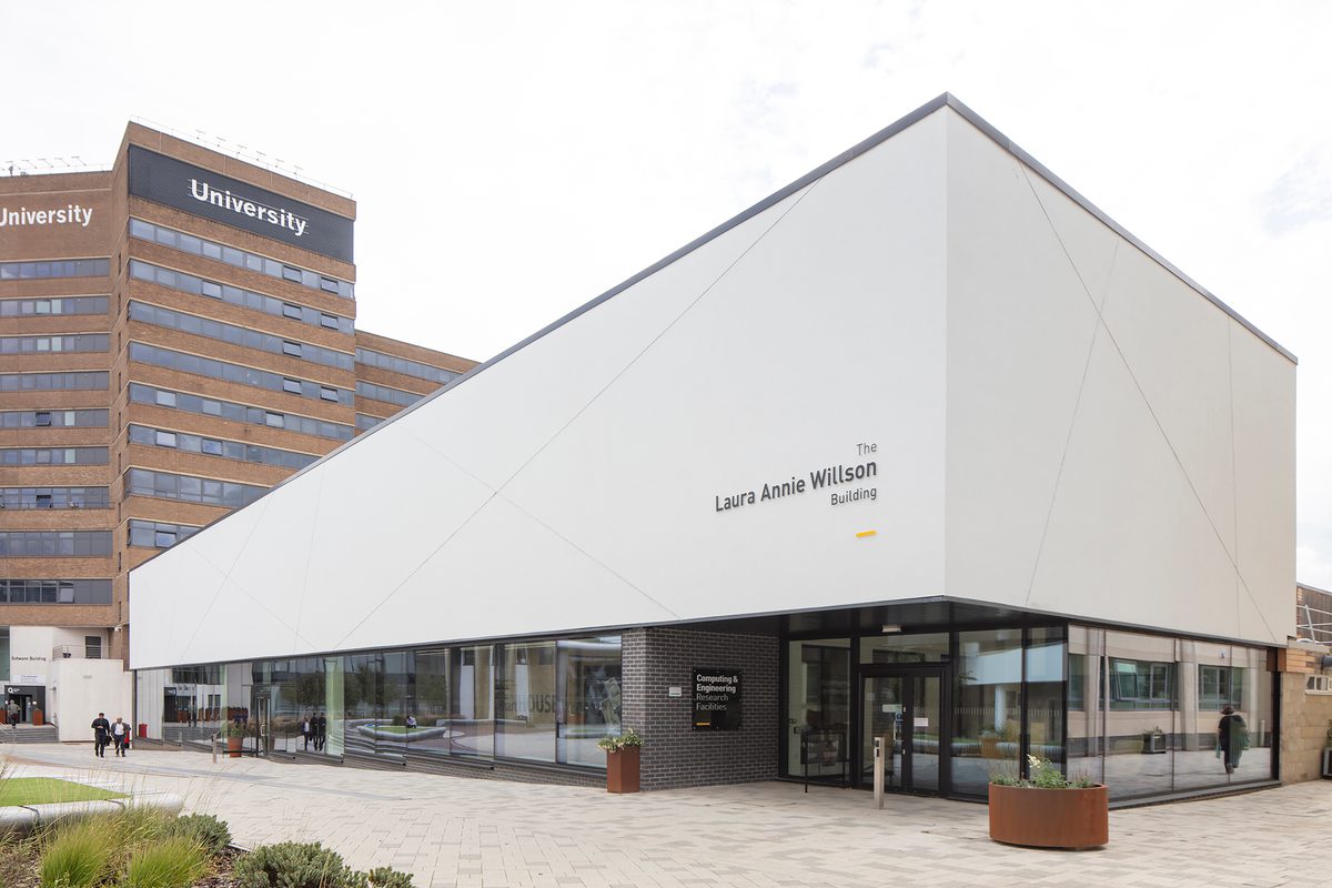 The front exterior of the Laura Annie Wilson Building, with highly glazed ground floor, the building name on the side of the building, surrounded by landscaped public realm.