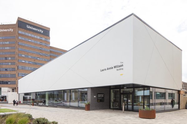 The front exterior of the Laura Annie Wilson Building, with highly glazed ground floor, the building name on the side of the building, surrounded by landscaped public realm.
