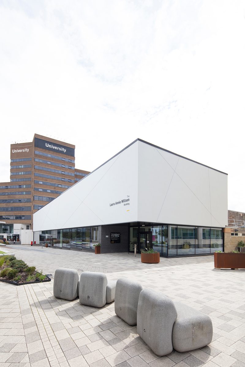 The front exterior of the Laura Annie Wilson Building, with highly glazed ground floor, the building name on the side of the building, surrounded by landscaped public realm.