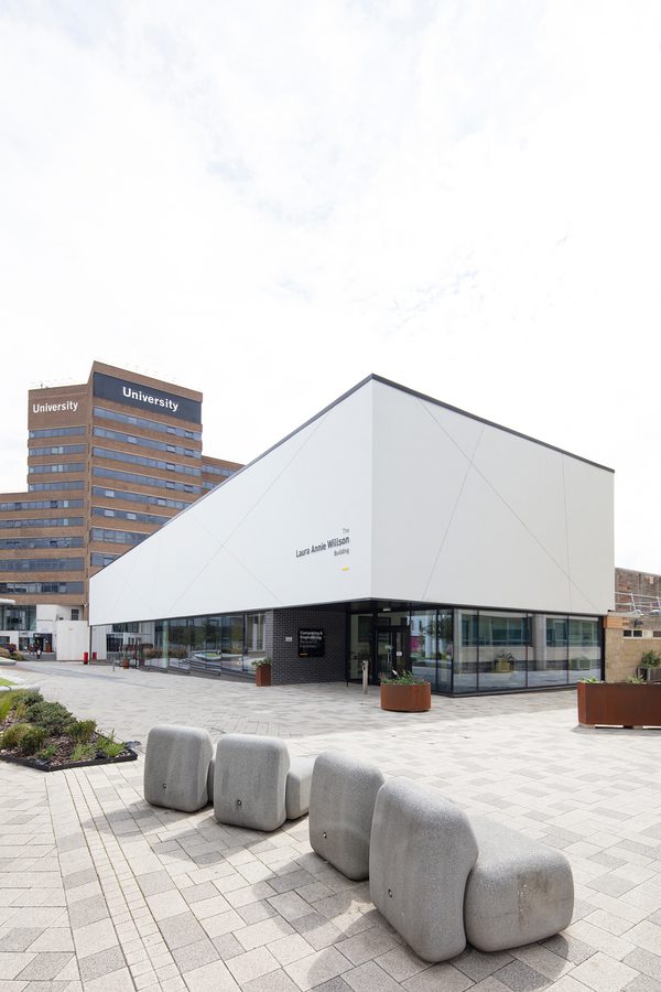 The front exterior of the Laura Annie Wilson Building, with highly glazed ground floor, the building name on the side of the building, surrounded by landscaped public realm.