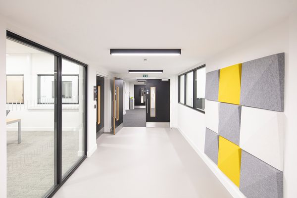 A bright circulation space within the Laura Annie Wilson building, with floor to ceiling glazed, internal windows and decorative yellow, grey and white wall features.