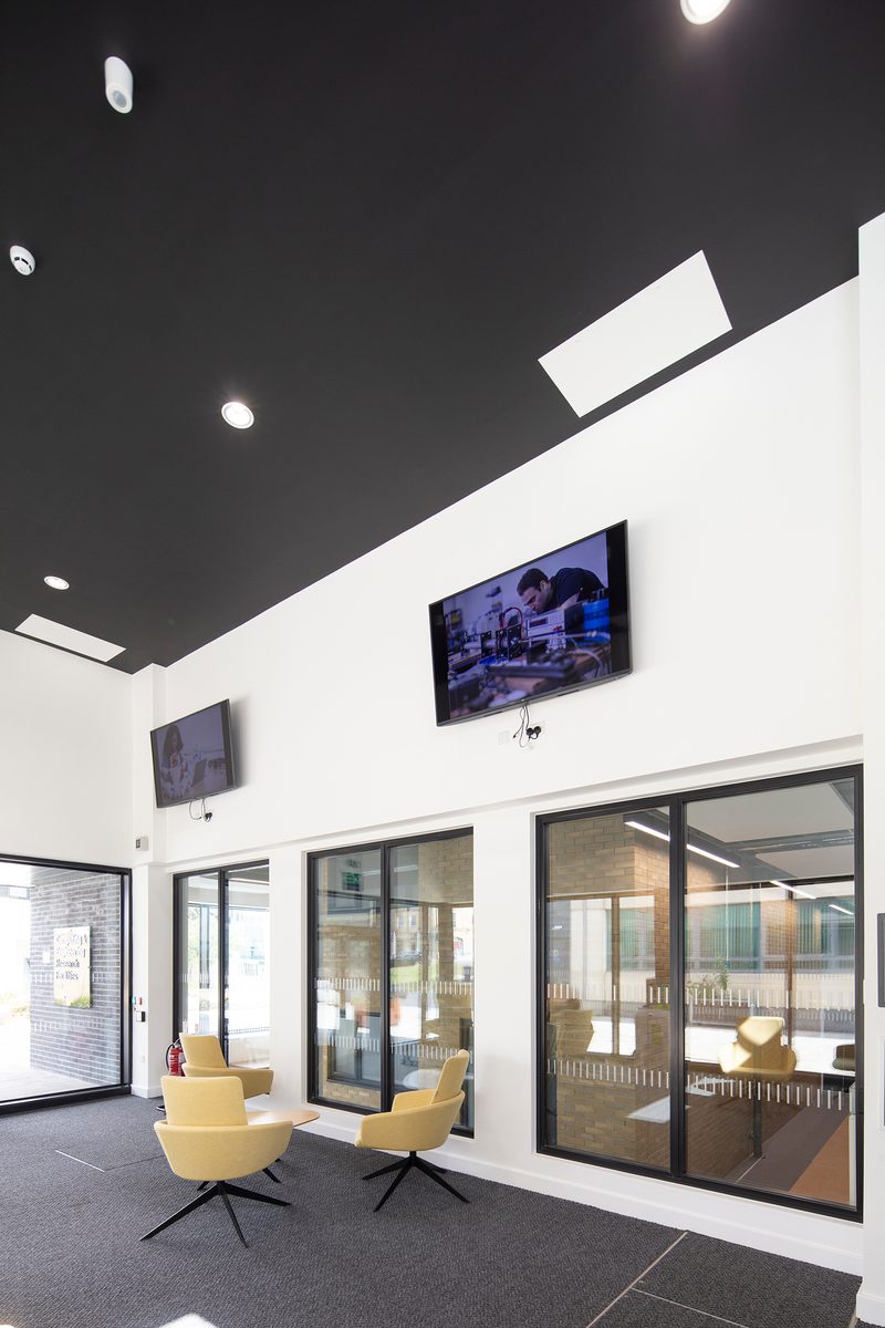 A double height interior communal space within the Laura Annie Wilson Building, with seating and floor to ceiling windows on the ground floor.