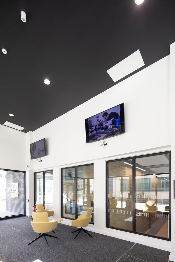A double height interior communal space within the Laura Annie Wilson Building, with seating and floor to ceiling windows on the ground floor.