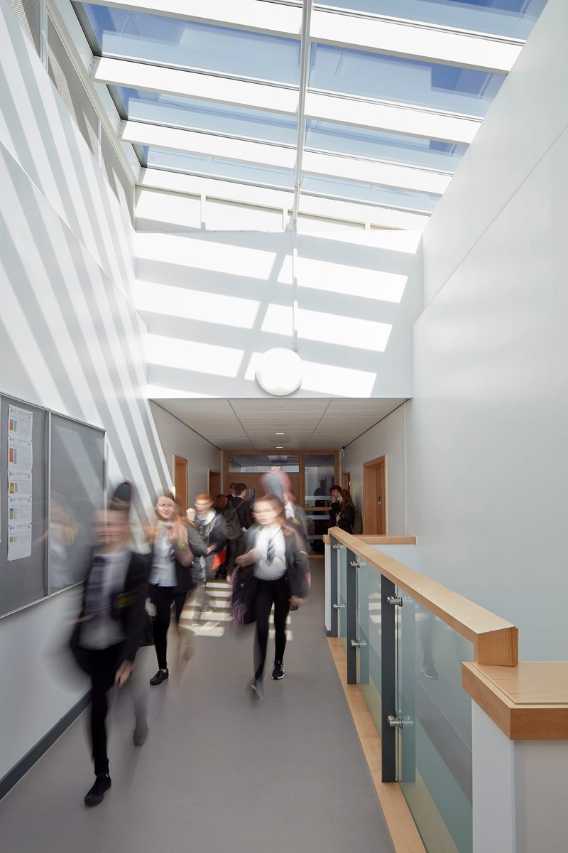 Students walking through a bright circulation space in Levenmouth campus, with slanted, glazed roof lights.