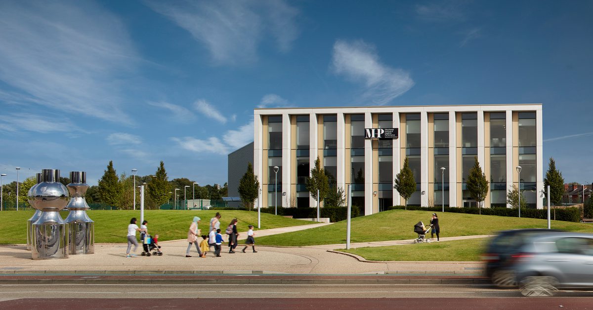 Pedestrians using the green public realm in front of the Manchester Institute of Health and Performance.