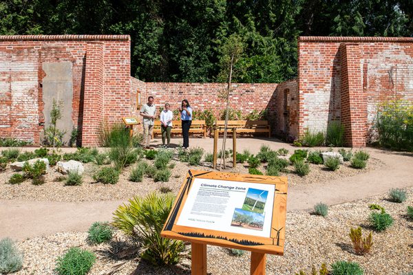 An information leaflet sat atop a wooden podium overlooking the vast nature park and garden at the University of Reading with a group of visitors exploring the space in the background.