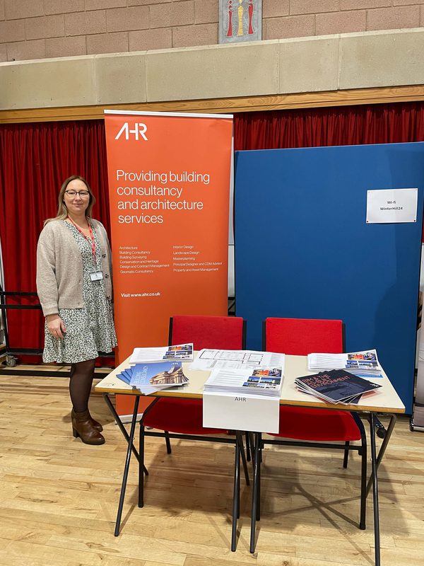 Architectural technologist Justina Wilson stood smiling next to an AHR pull up banner at a college careers fair.
