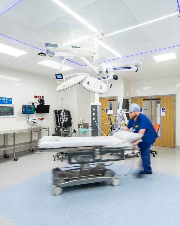 A portrait view of the operating theatre inside the Princess Royal Hospital Day Case Elective Hub with an NHS colleague pushing an empty gurney surrounded by modern equipment.