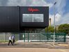 Pedestrains walking past a black exterior corner of Polyseam Manufacturing Unit with bright red logo graphics on the wall.