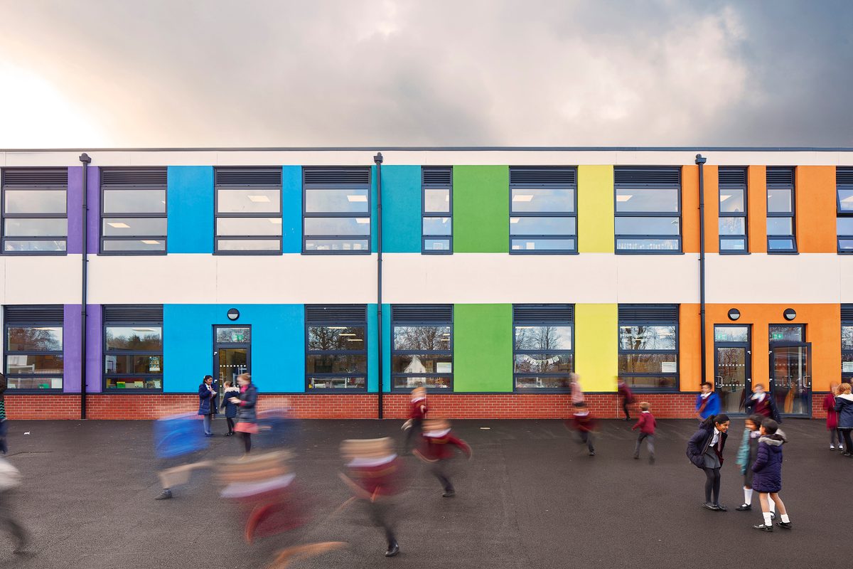 Children playing in the outdoor area of Pound Hill Junior School, with the school's bright, colourful facade in the background.