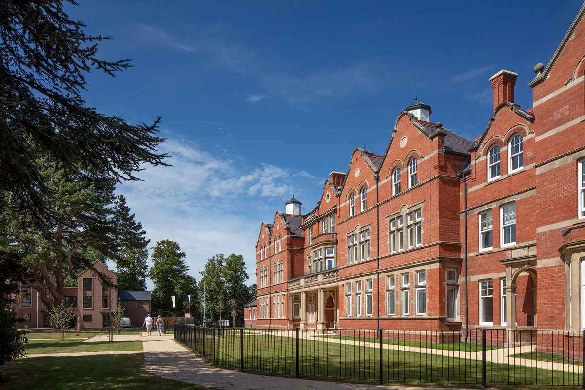An exterior shot of the Radbrook Village development, with residents enjoying the communal green space surrounding the ornate detailing of the refurbished Radbrook Hall and adjoining new build homes.