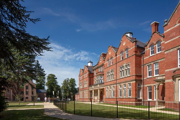 An exterior shot of the Radbrook Village development, with residents enjoying the communal green space surrounding the ornate detailing of the refurbished Radbrook Hall and adjoining new build homes.