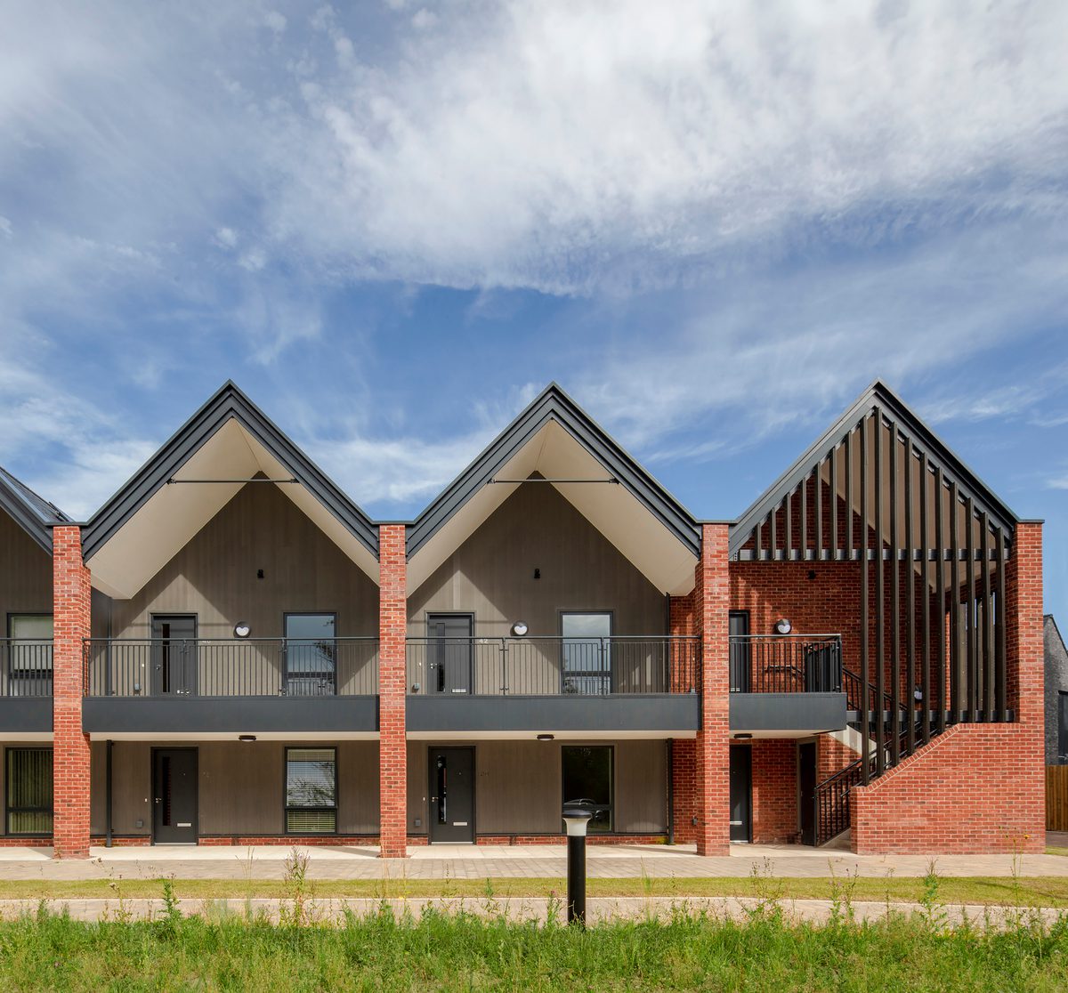 A front view of a row of new build homes, with gabled rooves and integrated balconies and surrounding green space, part of the Radbrook Village development.