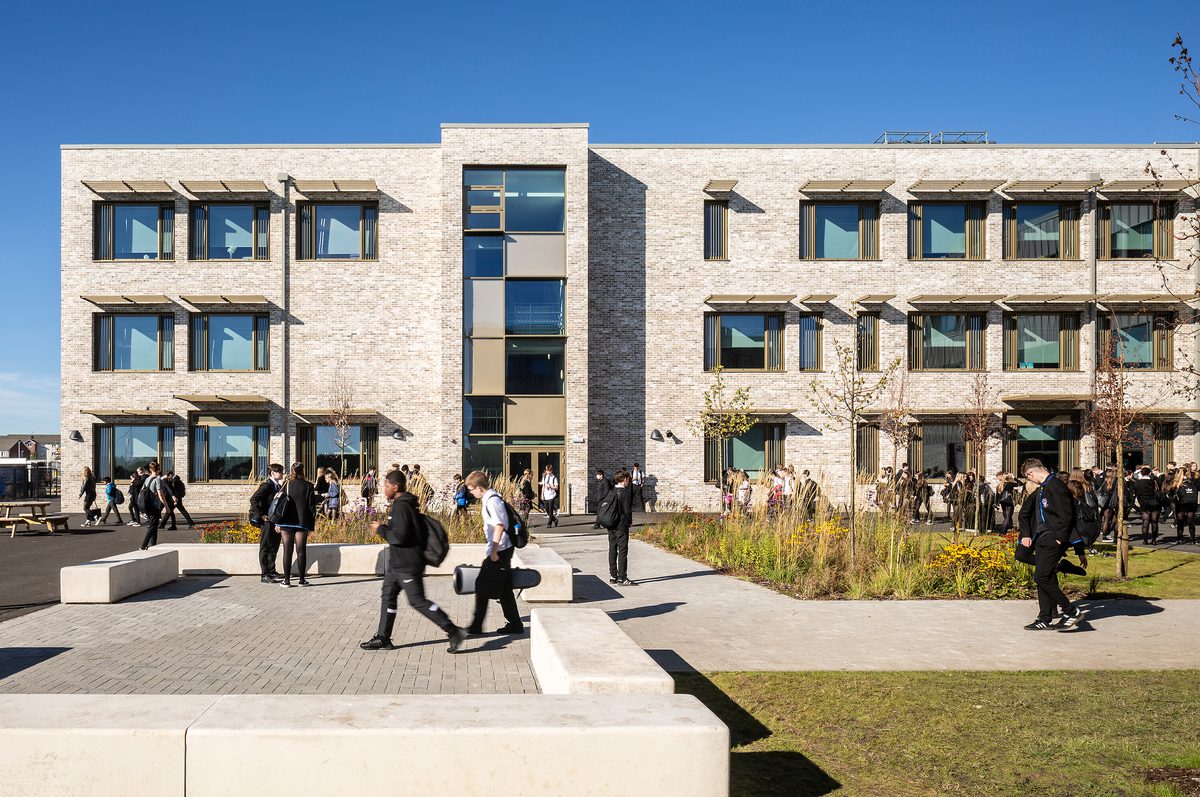 Pupils using the shared outdoor space of the Woodmill and St Columba's RC High School, with seating areas, extensive landscaping and plating, and the school exterior facade in the background.