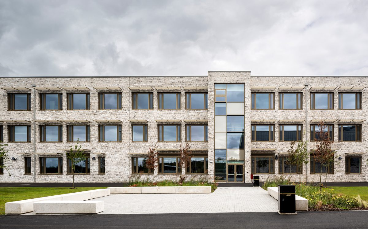 An exterior wall of the Woodmill and St Columba's RC High School, showing the large scale of the school, shading fins above each window, and landscaped planting surrounding the school.