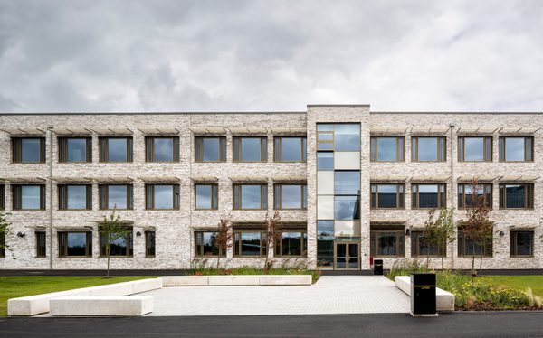 An exterior wall of the Woodmill and St Columba's RC High School, showing the large scale of the school, shading fins above each window, and landscaped planting surrounding the school.