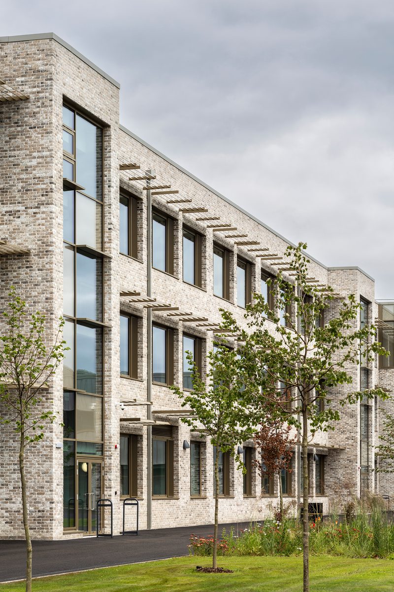 An exterior wall of the Woodmill and St Columba's RC High School, showing the large scale of the school, shading fins above each window, and landscaped planting surrounding the school.