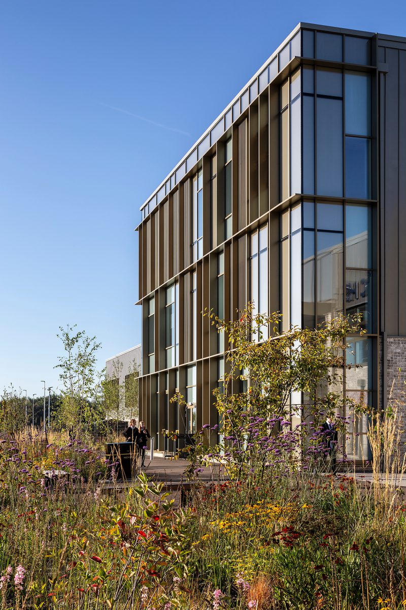 Exterior of Woodmill and St Columba's RC High School with glazed frontage and large amounts of greenery and planting in a landscaped area in front of the building.