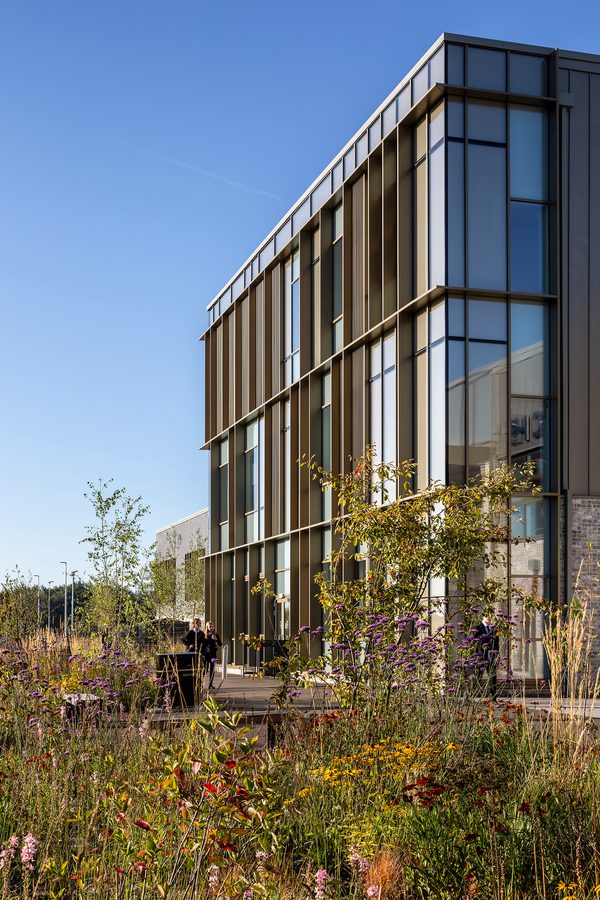 Exterior of Woodmill and St Columba's RC High School with glazed frontage and large amounts of greenery and planting in a landscaped area in front of the building.