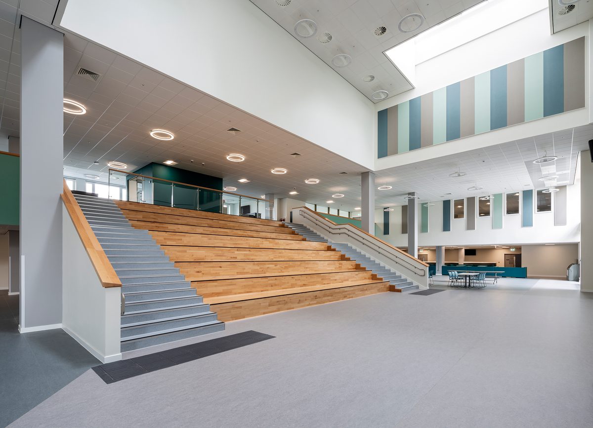 The large, open interior dining hall of the Woodmill and St Columba's RC High School, showing the Spanish steps, bespoke light features, natural materials and muted colour scheme.