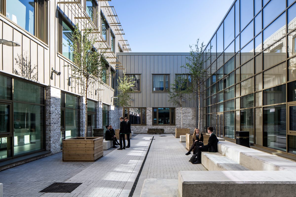 Pupils enjoying the outdoor space within the shared central courtyard within the Woodmill and St Columba's RC High School, with a double height glazed wall behind them.
