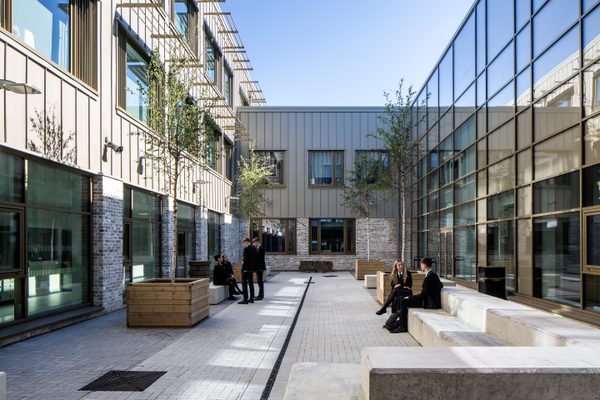 Pupils enjoying the outdoor space within the shared central courtyard within the Woodmill and St Columba's RC High School, with a double height glazed wall behind them.