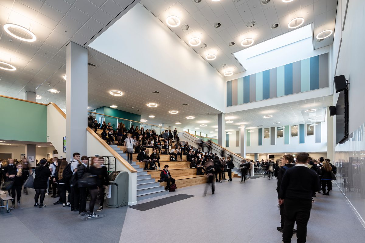 Pupils sitting on the Spanish Steps and using the surrounding space in the dining hall of the Woodmill and St Columba's RC High School.
