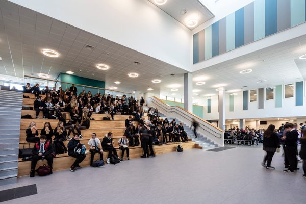 Pupils sitting on the Spanish Steps and using the dining hall of the Woodmill and St Columba's RC High School, with bespoke light features above and muted colour palette decorating the walls.