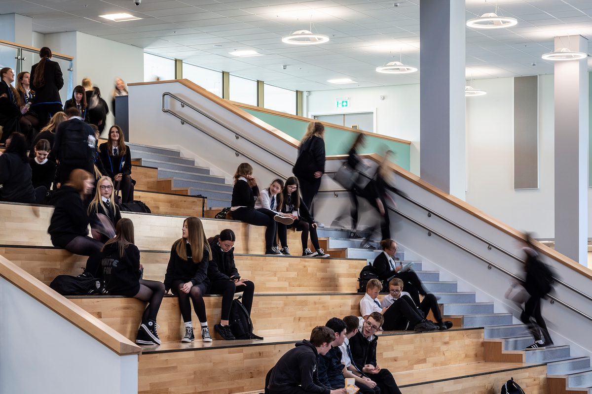 A detailed shot of pupils sitting on the Spanish Steps, with wood detailing, in the dining hall of the Woodmill and St Columba's RC High School.