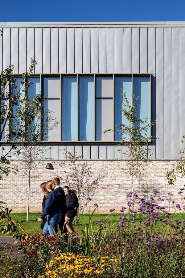 Pupils walking through the communal landscaped exterior of the Woodmill and St Columba's RC High School, with the school in the background and biodiverse planting in the foreground.