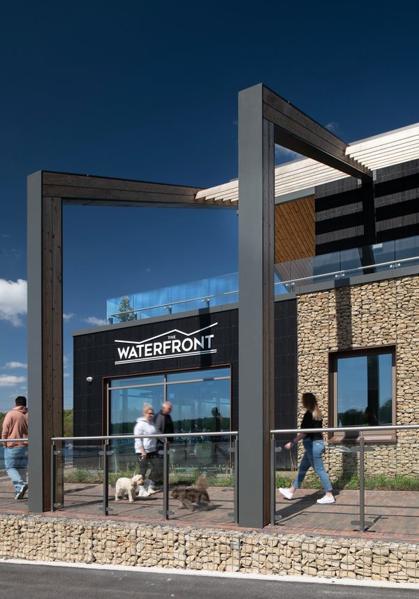 People walking on a pathway in front of the Rother Valley Country Park visitor centre with stone walls and signage in the background.