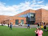 Pupils playing in the green outdoor space outside of Sacred Heart Primary School on a bright day.