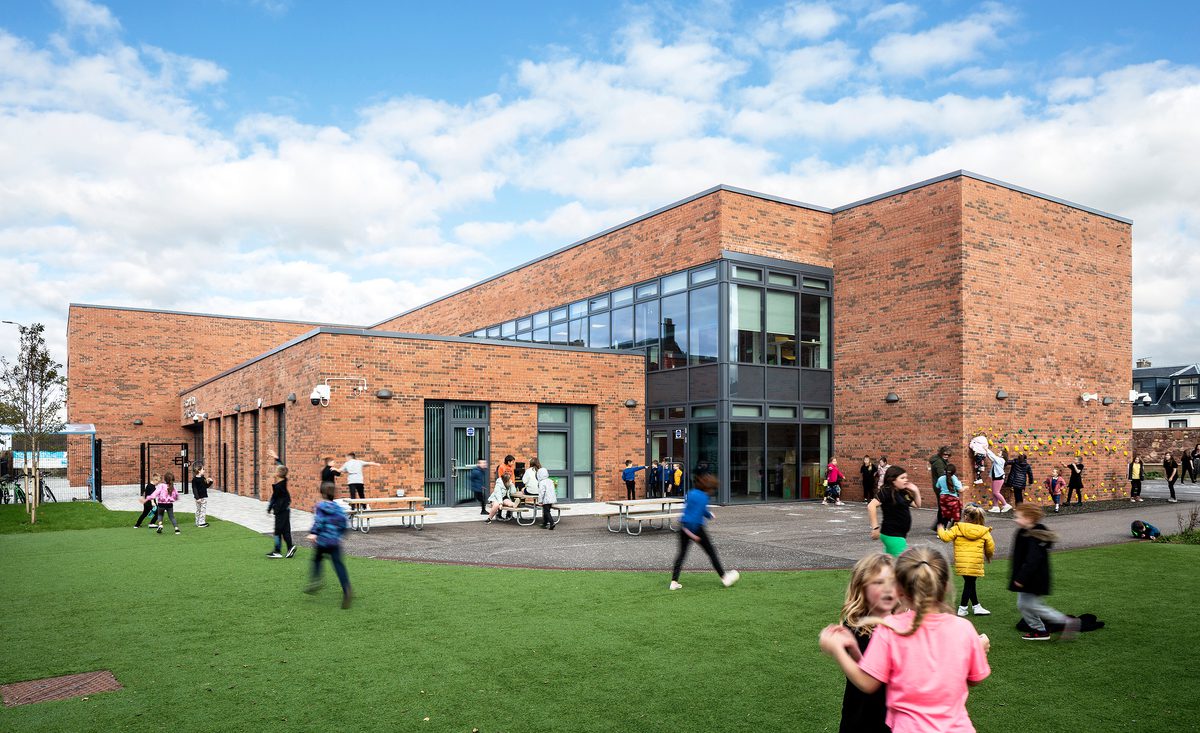 Pupils playing in the green outdoor space outside of Sacred Heart Primary School on a bright day.