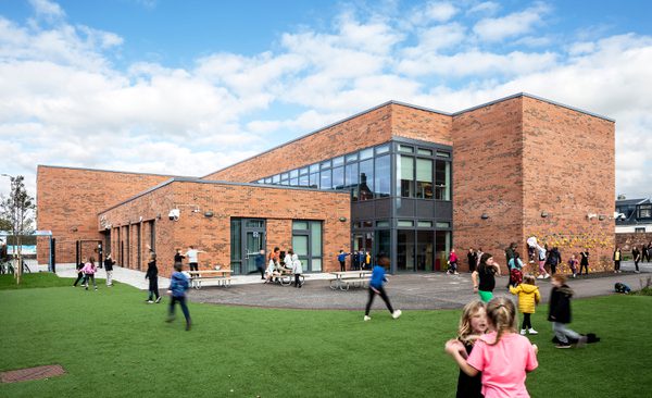 Pupils playing in the green outdoor space outside of Sacred Heart Primary School on a bright day.