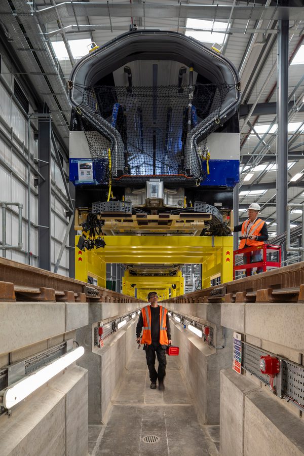 A person walking underneath a train in manufacture within a large interior hall at Siemens Mobility Train Manufacturing Facility.