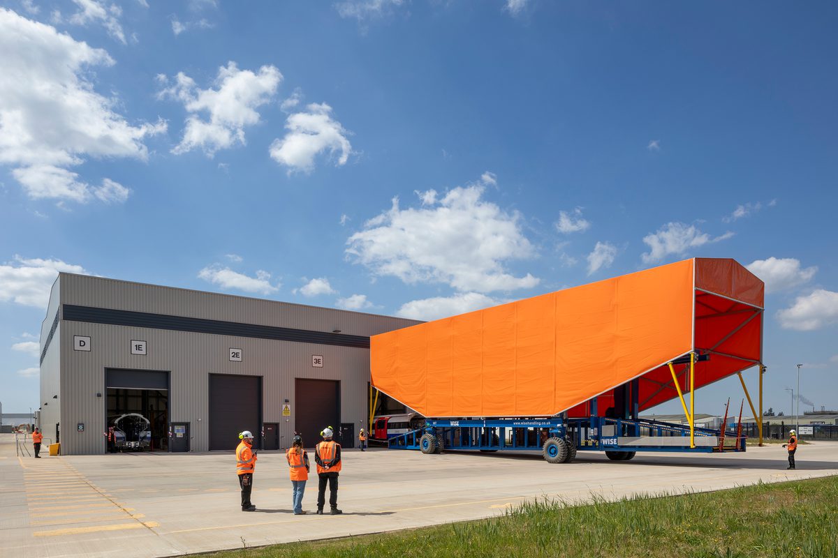 The outdoor yard at Siemens Mobility Train Manufacturing Facility, with a large, orange train cover connecting to the building.