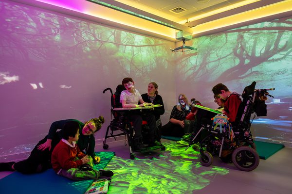 SEND students interacting with teachers in a sensory room with various colours and patterns around them.